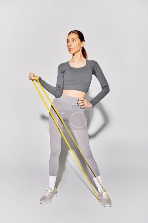Photo for A sporty young woman in active wear working out with elastics against a grey background. - Royalty Free Image