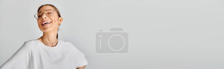 Foto de Una joven con gafas y una camisa blanca posa sobre un fondo gris, exudando una sensación de calma y confianza. - Imagen libre de derechos