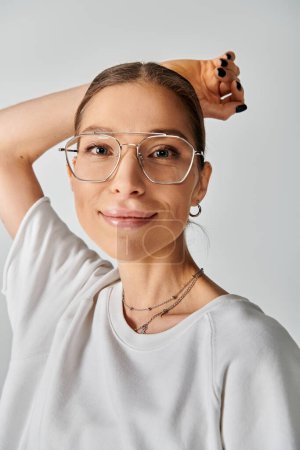 A young woman in a white shirt and glasses on a grey background, exuding elegance and style with her chic look.
