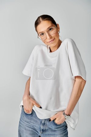 A young woman in a white t-shirt and glasses poses on a grey background, exuding elegance and confidence.