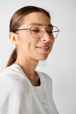A young woman with glasses and a white shirt poses on a grey background, exuding intelligence and style.