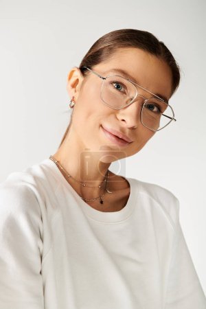 Foto de Una joven con gafas y una camisa blanca emana una sensación de calma sobre un fondo gris. - Imagen libre de derechos