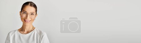 Foto de Una joven con gafas y camisa blanca posa sobre un fondo gris. - Imagen libre de derechos