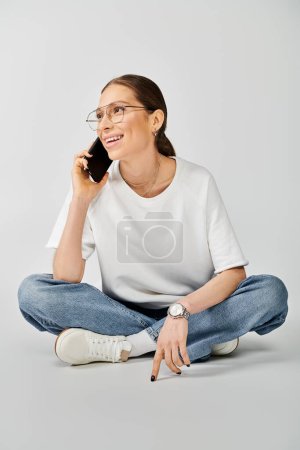 A woman in a white t-shirt sitting on the floor, engaged in a phone call.