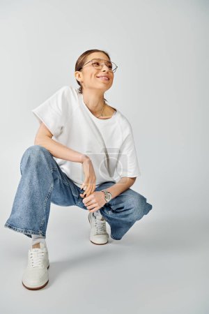 A young woman in a white shirt and jeans striking a pose against a grey background.