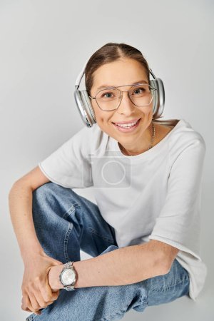 Eine junge Frau in weißem T-Shirt und Brille sitzt auf dem Boden und ist mit Kopfhörern in Musik getaucht..