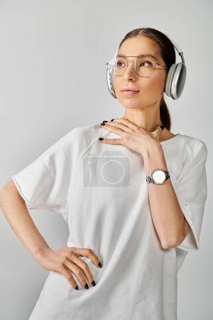 A young woman in a white shirt listens to music through headphones against a grey background.