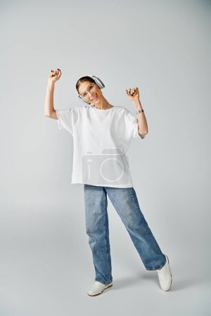 A stylish young woman in a white shirt and jeans strikes a pose against a neutral grey background.