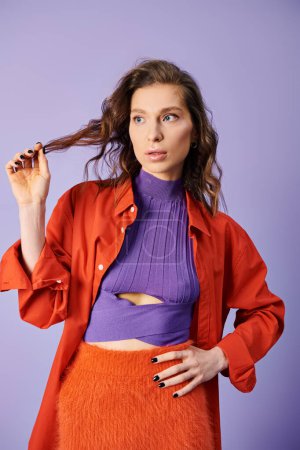 Stylish young woman radiates elegance in a purple top and orange skirt against a vibrant purple background.