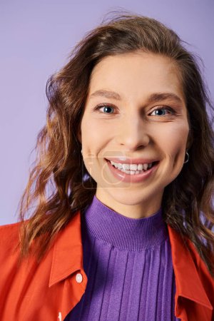 A stylish young woman stands out in a vibrant orange jacket against a purple background.