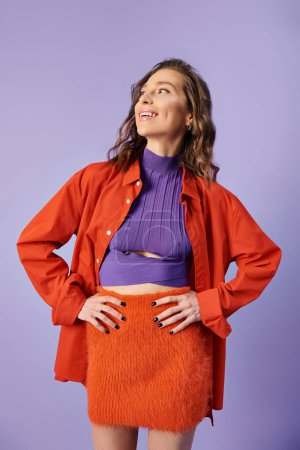 A stylish young woman wearing an orange skirt and a purple top poses against a vibrant purple background.