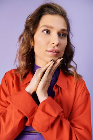 A stylish young woman in a vibrant orange jacket striking a pose on a purple background.