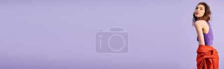 Téléchargez les photos : Jeune femme élégante dans un haut violet et un pantalon rouge, respirant la confiance et le flair sur un fond violet vibrant. - en image libre de droit