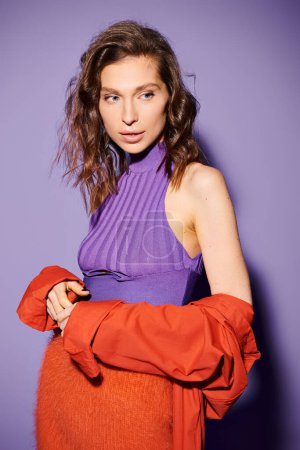 A stylish young woman confidently showcasing a vibrant orange skirt paired with a purple top on a purple background.