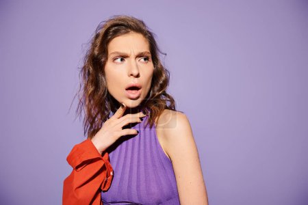 Photo for A stylish young woman with a surprised look on her face, dressed in vibrant orange attire against a purple background. - Royalty Free Image