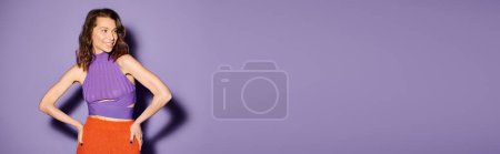 Téléchargez les photos : Jeune femme élégante en tenue orange vif debout en toute confiance devant un mur violet frappant. - en image libre de droit