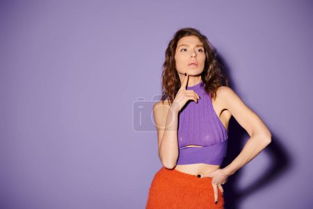 A stylish young woman showcasing a vibrant orange skirt and a purple top against a bold purple backdrop.