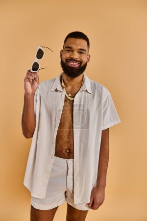 Un homme dans une chemise blanche croquante tient doucement une paire de lunettes de soleil élégantes, exsudant un sentiment de calme et de sophistication.