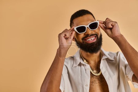 Un homme avec une barbe élégante et des lunettes de soleil à la mode respire la confiance et le charisme alors qu'il pose pour la caméra.