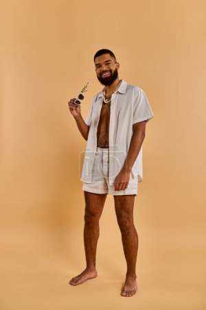A stylish man in a white shirt and shorts strikes a pose while confidently holding a pipe in his hand.