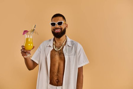 A stylish man wearing sunglasses holds a glass of juice, exuding relaxation and enjoyment under the suns rays.
