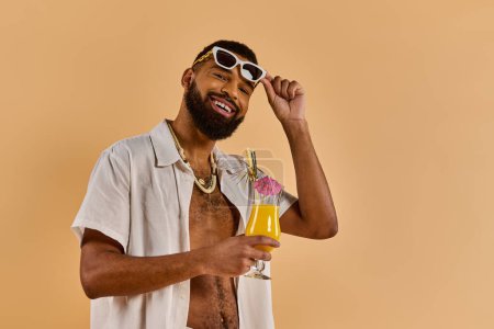 Un hombre con estilo protegido por gafas de sol de moda sostiene una bebida fresca en su mano, exudando un ambiente relajado y seguro de sí mismo mientras disfruta de su bebida.