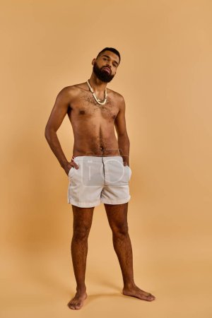 Un hombre sin camisa de pie con confianza delante de un fondo bronceado, mostrando su físico muscular y sentido de seguridad.