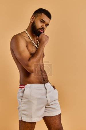 Un hombre con la barba llena con confianza posa delante de la cámara, mostrando su físico sin camisa. Exuda fuerza y masculinidad.