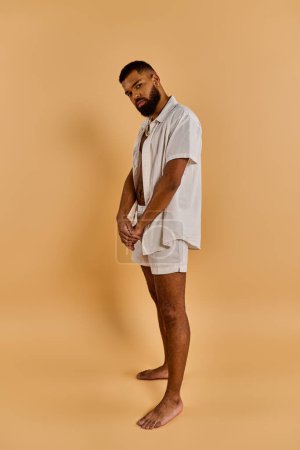 Photo for A man clad in a crisp white shirt and comfortable shorts stands in a serene setting, soaking up the warmth of the sun. - Royalty Free Image