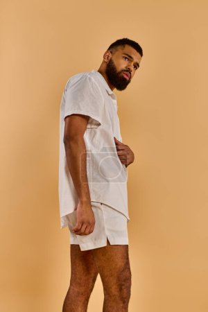 Foto de Un hombre con una camisa blanca y pantalones cortos está de pie con confianza, mostrando atletismo y gracia en su postura equilibrada. - Imagen libre de derechos