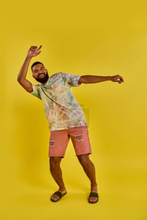 A man wearing a vibrant tie dye shirt paired with pink shorts, exuding a laid-back and colorful aura in his outfit choice.