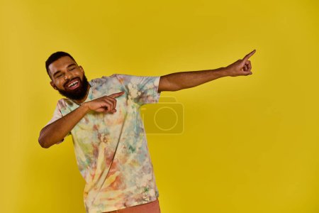 A man wearing a vibrant tie dye shirt points animatedly at something out of frame, his colorful attire standing out against a neutral backdrop.