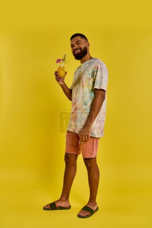 Foto de Un hombre se para confiadamente frente a un vibrante telón de fondo amarillo, sosteniendo una bebida delicadamente en su mano mientras mira hacia adelante. - Imagen libre de derechos