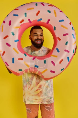 Foto de Un hombre se esconde juguetonamente detrás de un enorme donut, mostrando su lado caprichoso y humorístico mientras disfruta de un sabroso manjar.. - Imagen libre de derechos