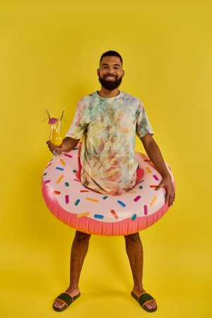 Téléchargez les photos : Un homme se détend sur un donut flottant dans un plan d'eau, tenant un verre dans sa main sous le soleil chaud. - en image libre de droit