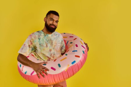 A man joyfully holding a massive donut in front of a vibrant yellow background, showcasing the sugary treat.