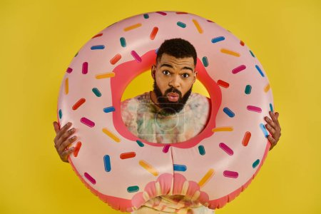 Photo for A man joyfully holds a massive pink donut covered in colorful sprinkles, showcasing a moment of whimsical delight and indulgence. - Royalty Free Image