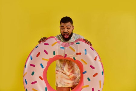 Un hombre con una sonrisa en la cara sosteniendo un enorme donut cubierto de coloridos salpicaduras, mostrando una sensación de alegría e indulgencia en un momento surrealista.