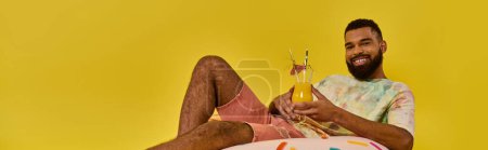 Photo for A man gracefully sits on a colorful beach ball, leisurely enjoying a glass of wine in a serene beach setting. - Royalty Free Image