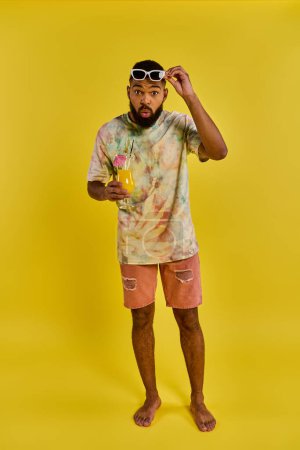 A stylish man in a vibrant tie dye shirt is holding a refreshing drink in his hand, exuding a carefree and relaxed vibe.