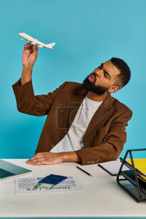 Un hombre se sienta en un escritorio, enfocado en una pantalla de computadora portátil mientras un avión modelo se sienta a su lado, mostrando su pasión por la aviación.