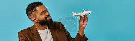 Ein Mann hält ein detailliertes Modell eines weißen Flugzeugs in der Hand, das kompliziertes Design und Handwerkskunst zeigt. Er blickt weg, verloren in Gedanken an Luftfahrt und Abenteuer.