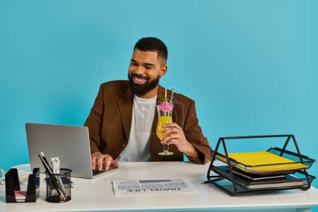 Un homme est assis à un bureau avec un ordinateur portable ouvert devant lui, accompagné d'un verre. Il semble concentré et engagé dans son travail.