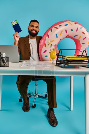 Foto de Un hombre sentado en un escritorio de madera, enfocado en su computadora portátil mientras disfruta de un delicioso donut con chispas. - Imagen libre de derechos