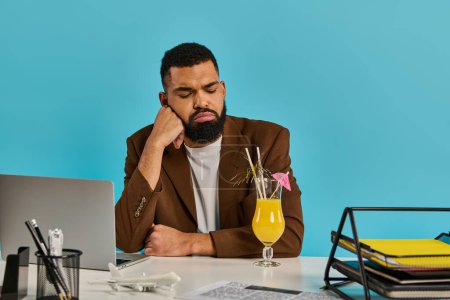 Téléchargez les photos : Un homme assis à un bureau, intensément concentré sur son écran d'ordinateur portable, avec une boisson rafraîchissante placée à côté de lui. - en image libre de droit