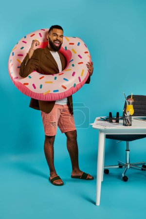 A man playfully holds a giant donut in front of his face, creating a whimsical and amusing sight. The colorful donut contrasts with his expression.