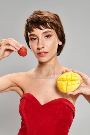 A young woman in a red dress holding a piece of fruit.