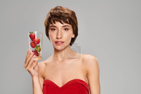 Young woman in red dress holds glass of strawberries.