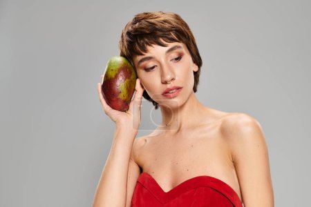 Elegant woman in red dress gracefully holding mango.