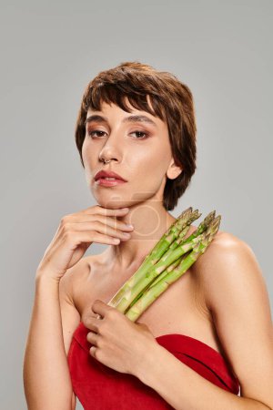 A young woman in a red dress gracefully holds a bunch of asparagus.